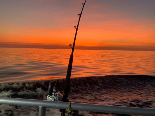 Single fishing pole on the side of boat with a beautifull orange sunset