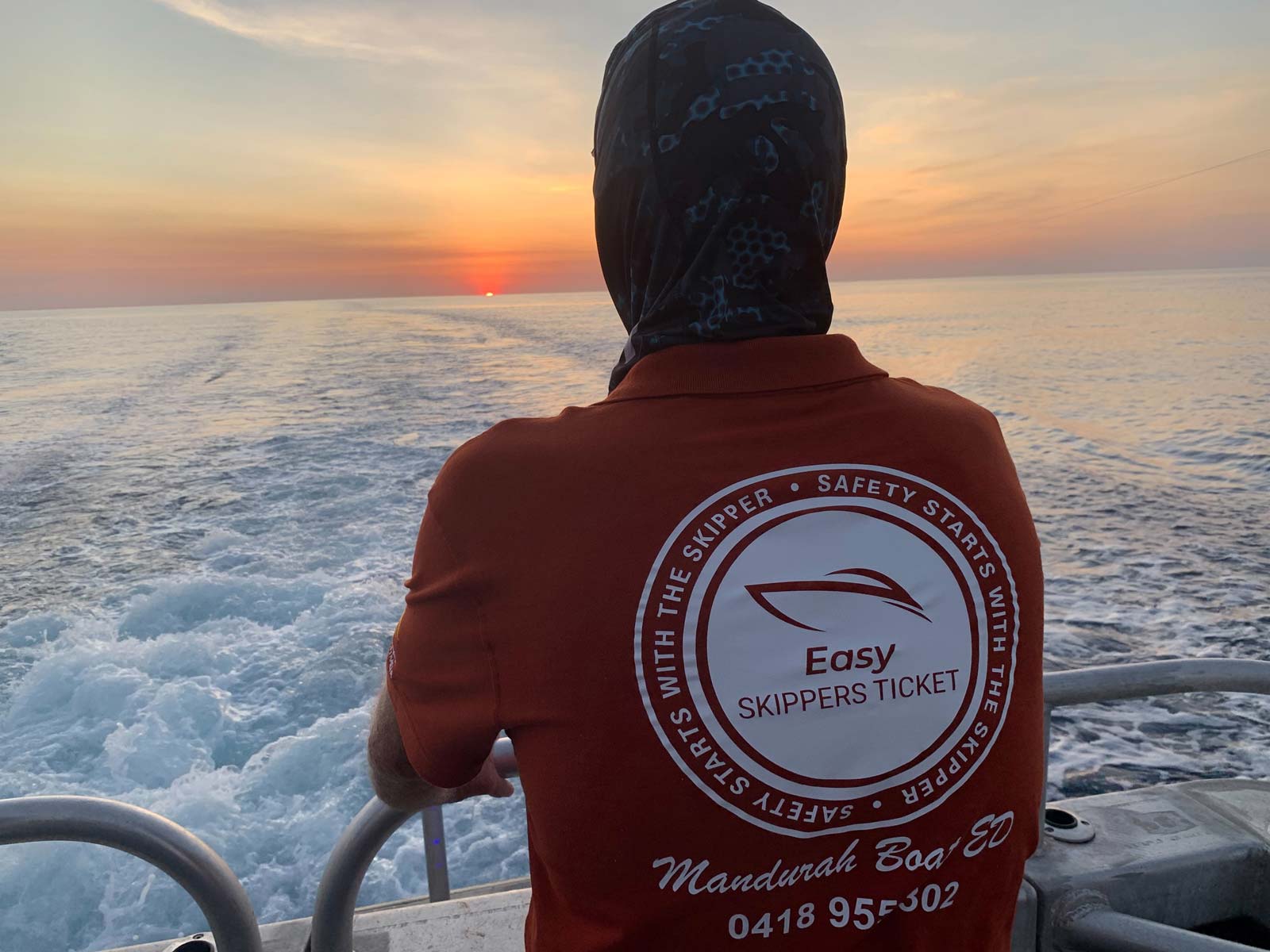 Brian Edwards at back of boat looking at the sunset wearing a tee shirt with Easy Skippers Ticket logo and phone number